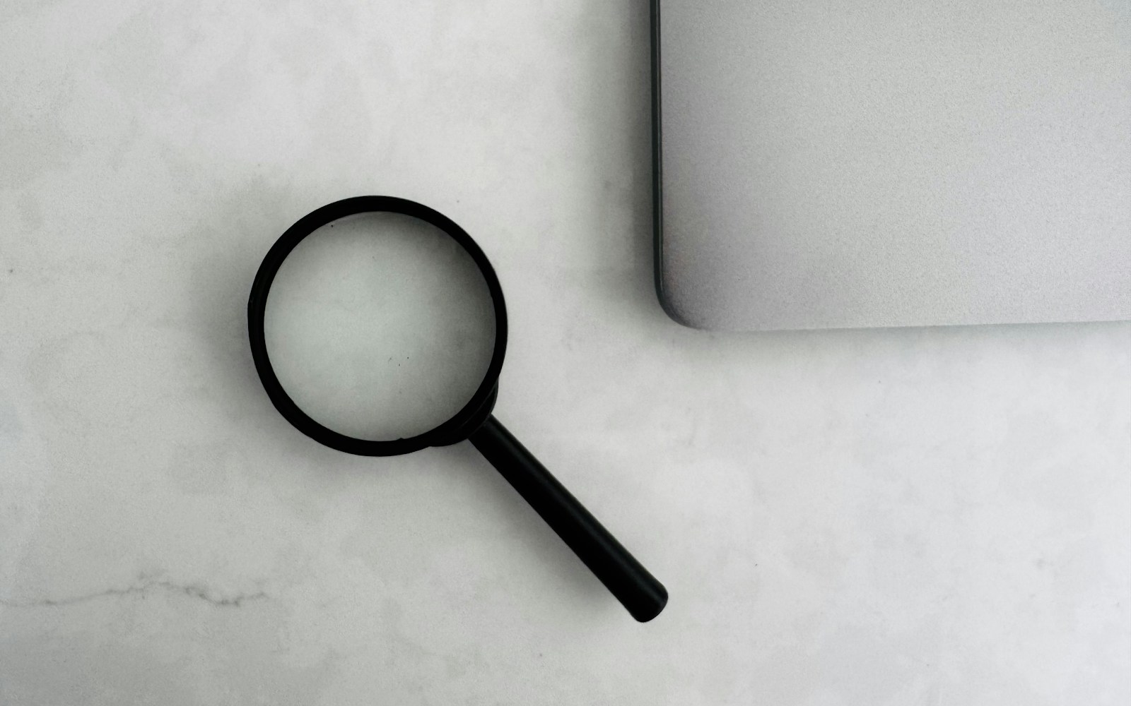 Magnifying glass sits near a laptop on a table.